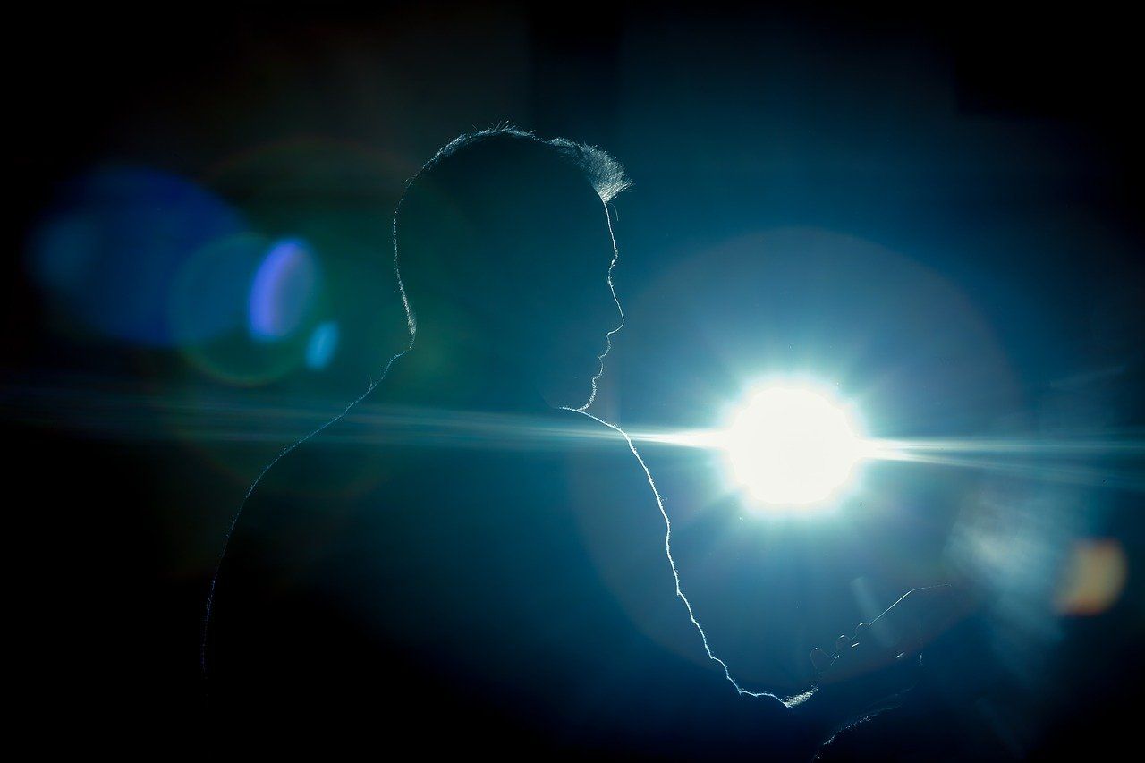Silhouette d'une personne se détachant sur une lumière bleu-blanc éclatante avec un effet de flare dans une scène sombre