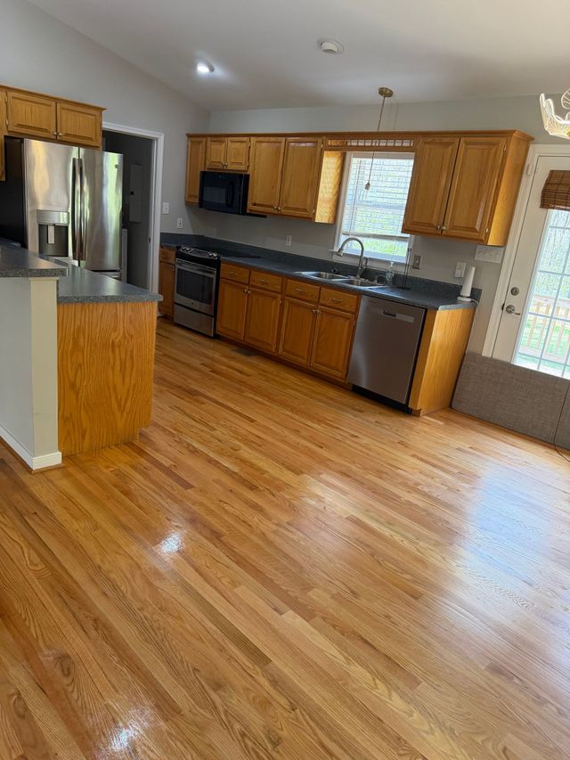 Bright kitchen with wood cabinets, stainless appliances, and hardwood floor, viewed from the dining area