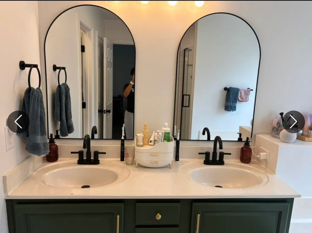 Double bathroom vanity with arched mirrors, black faucets, green cabinet, and towels hanging on the wall