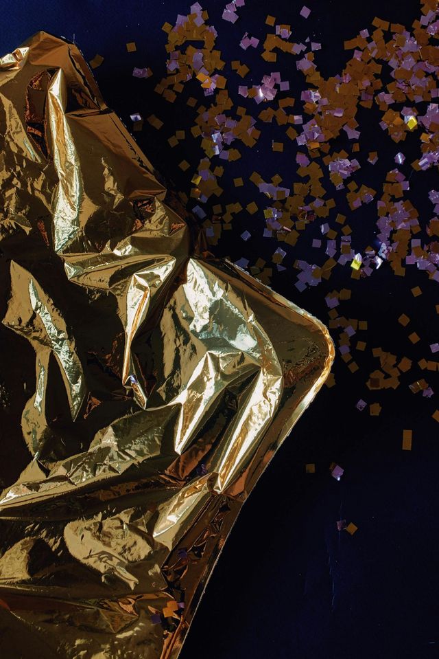 Gold foil sculpture with purple confetti against a dark background