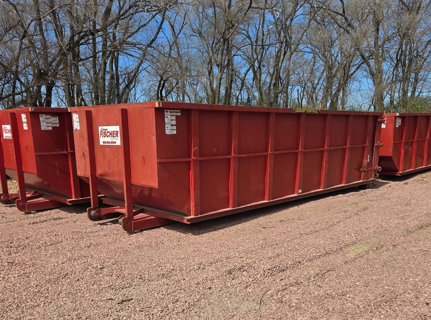 A large, empty blue dumpster sits on a dirt lot in front of a newly constructed suburban home.
