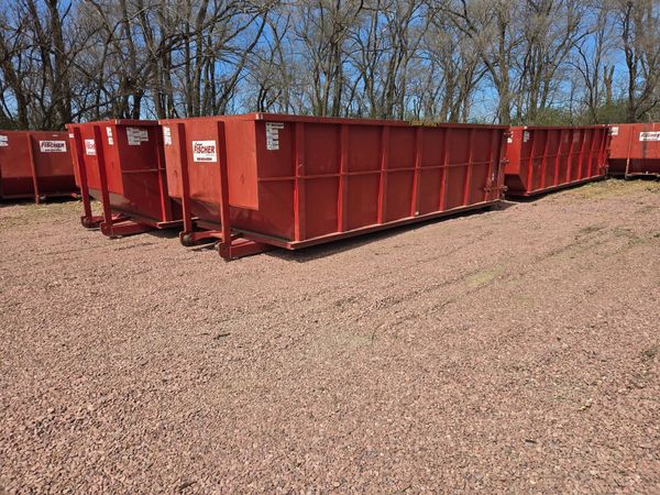 A large, empty blue dumpster sits on a dirt lot in front of a newly constructed suburban home.