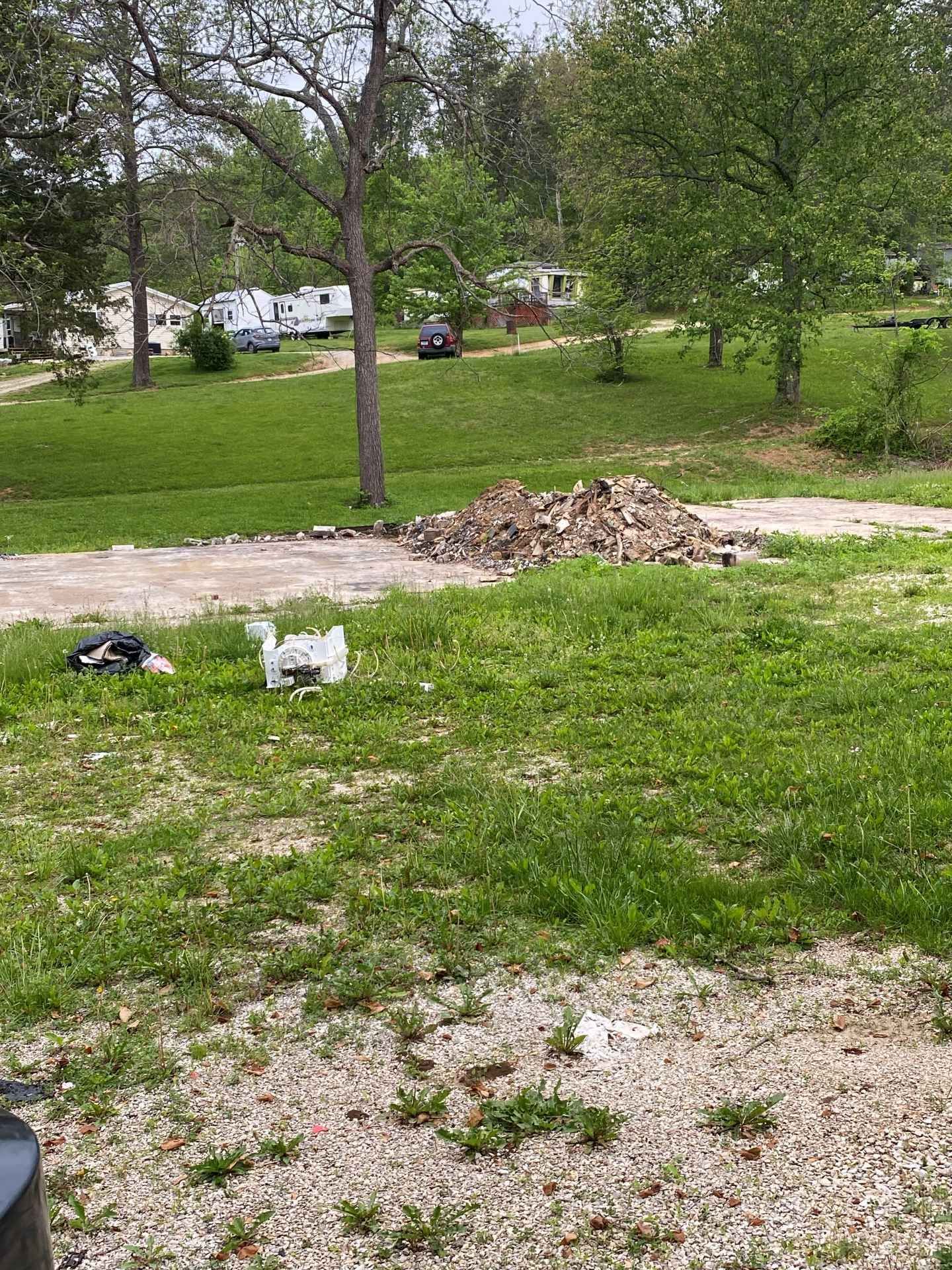 A white goose walks across a green lawn near a gravel driveway with a large pile of leaves in the background.