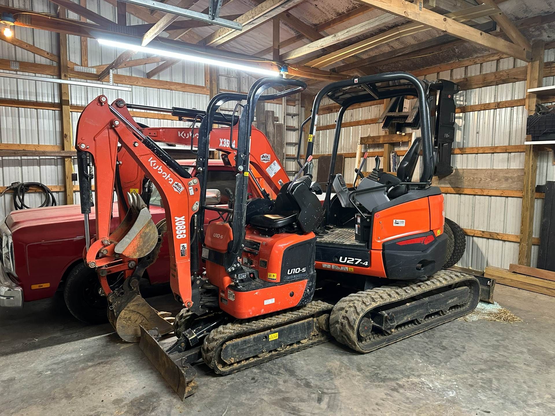 A bright orange Kubota mini excavator parked inside a wood-framed garage next to a red vehicle.
