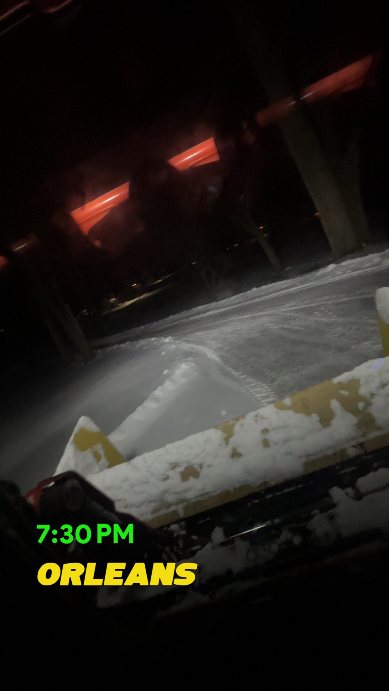Snow covers the ground at night in Orleans, viewed from inside a vehicle at 7:30 PM with a glowing red light visible.
