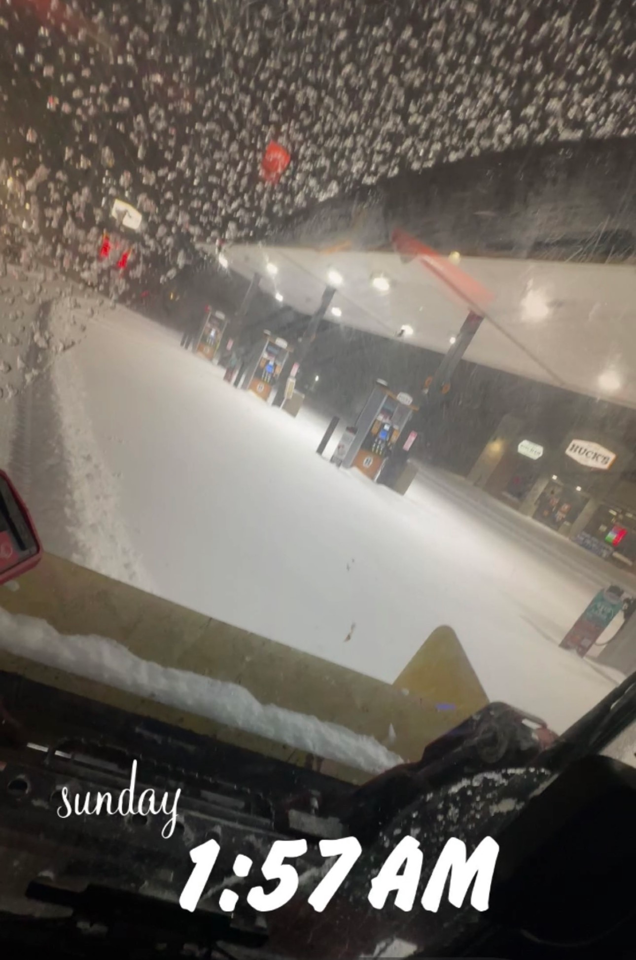 A snow-covered gas station at night, viewed from inside a vehicle, with the text 