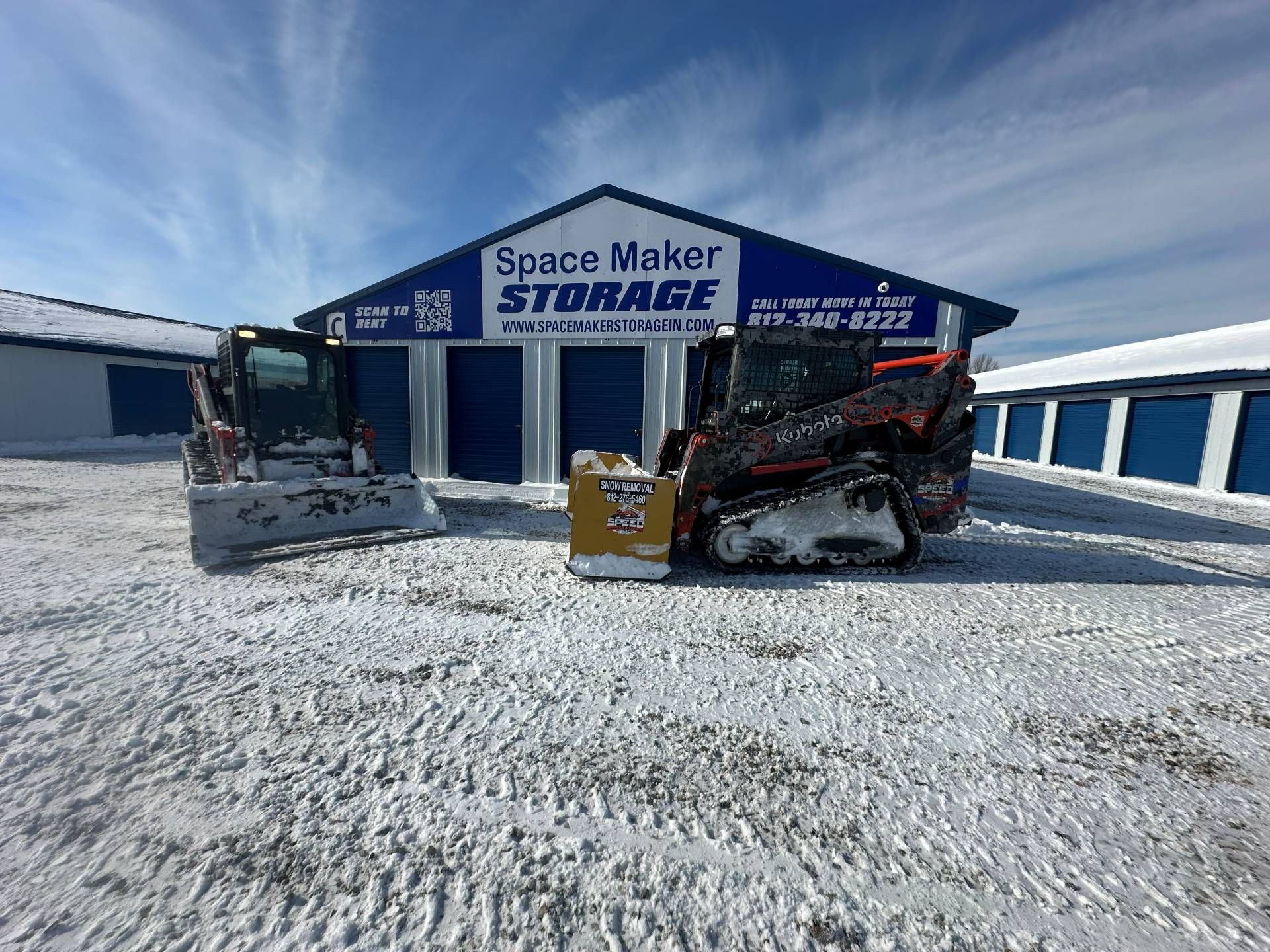 Two construction vehicles parked in front of a blue 
