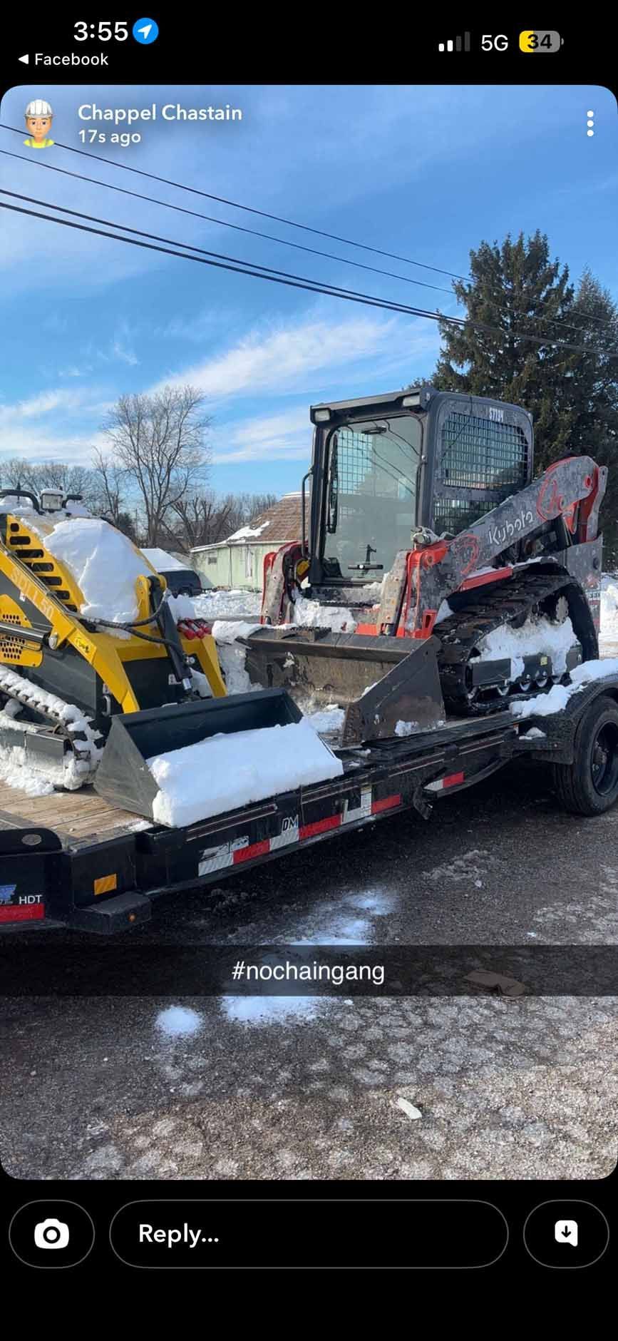 Two construction skid steers, one yellow and one orange, are loaded on a flatbed trailer outdoors on a sunny, snowy day.