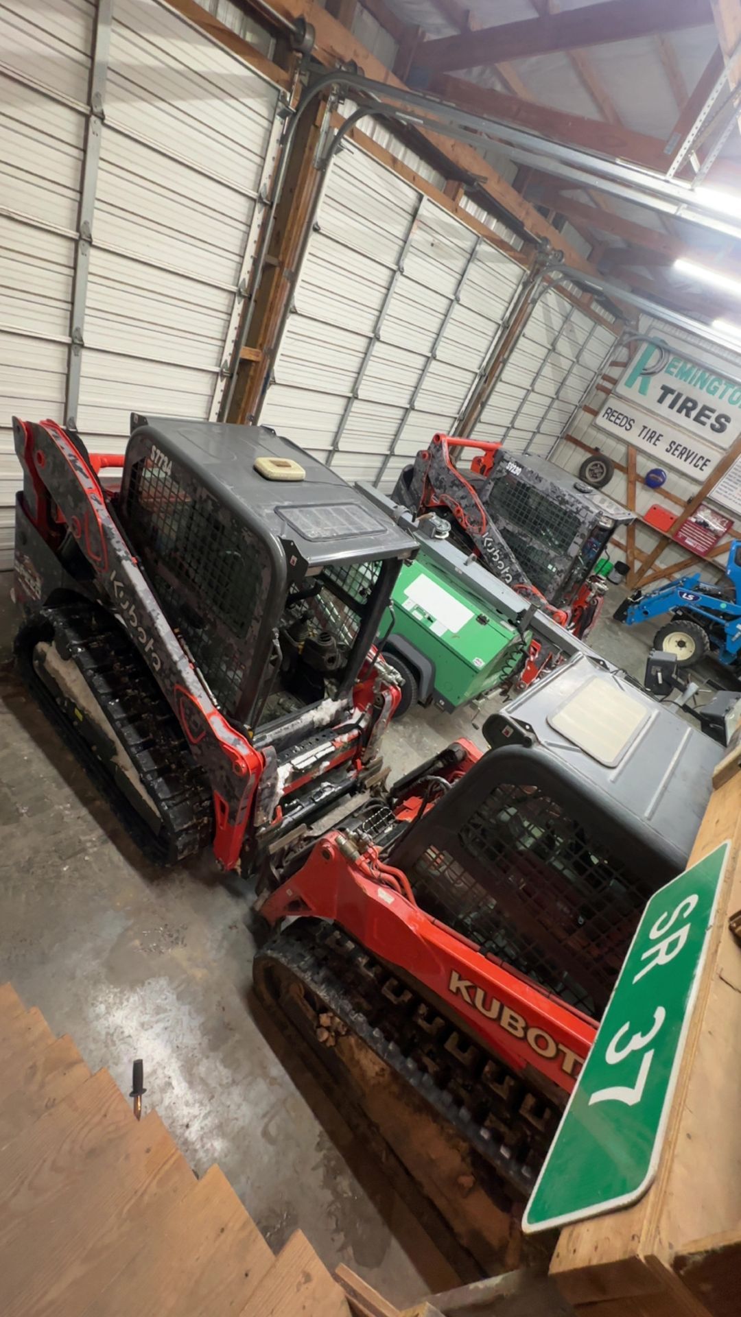 A garage housing two red Kubota track loaders, with a green 
