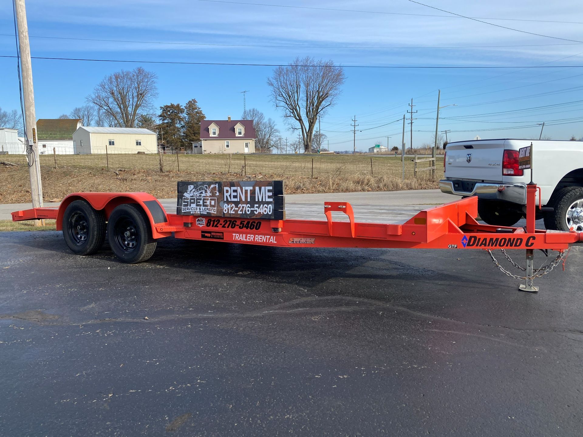 An orange Diamond C utility trailer sits in a parking lot next to a white pickup truck.