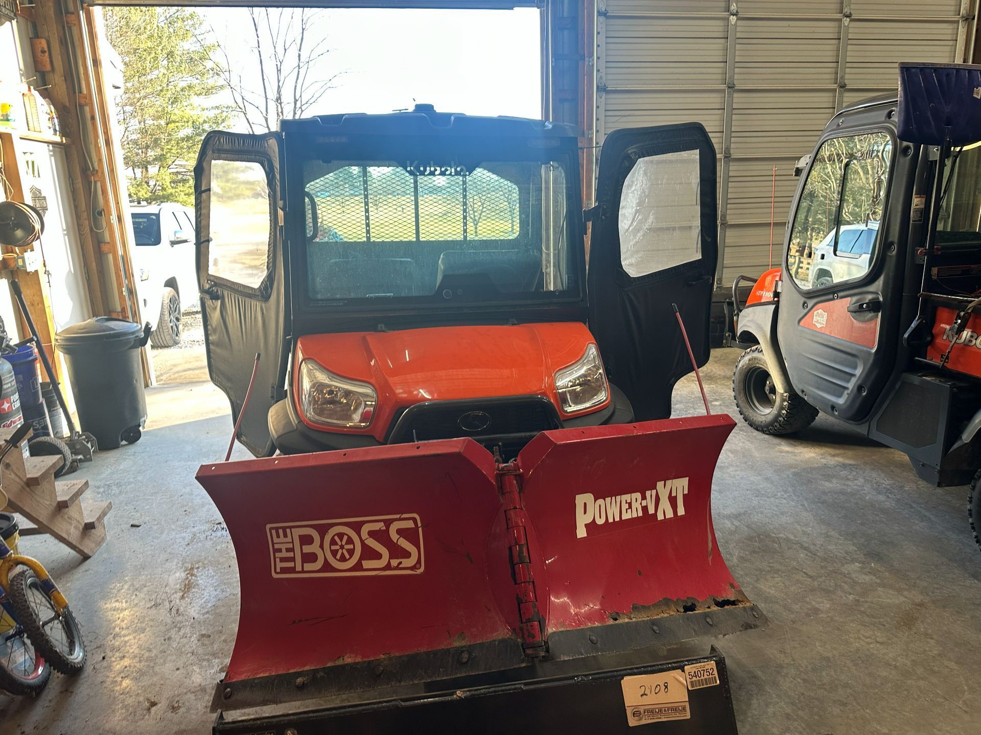 An orange utility vehicle with a red BOSS Power-V XT snow plow parked inside a garage.