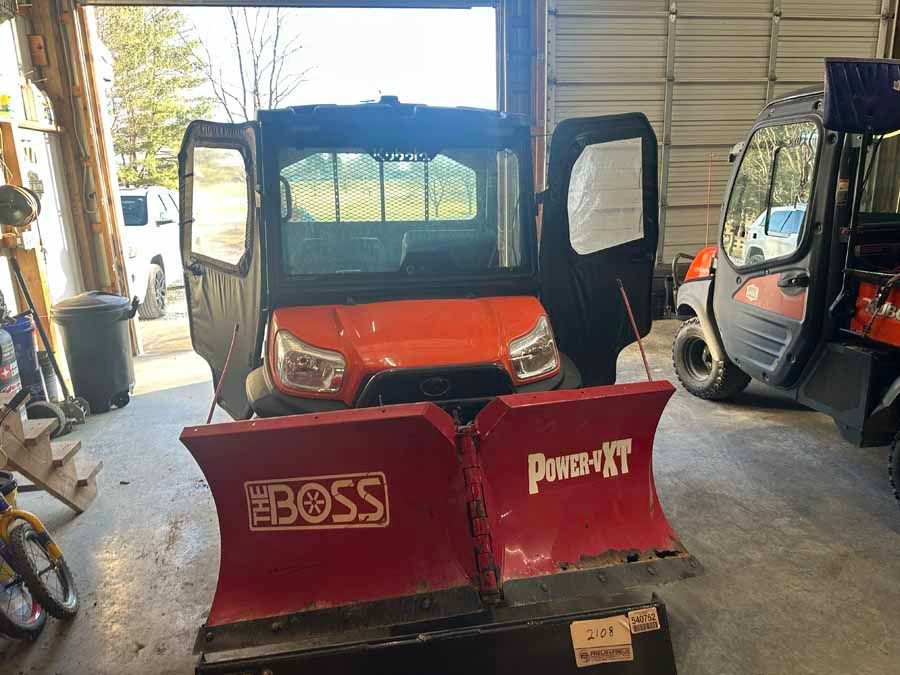 Orange UTV with a red BOSS Power-V XT snow plow attached, parked inside a garage.