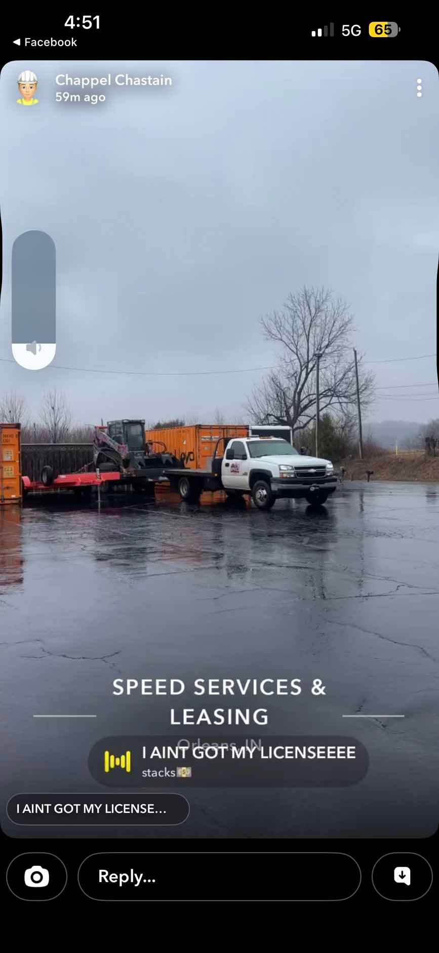 A white truck towing a trailer with construction equipment sits on a wet, paved lot under an overcast sky.