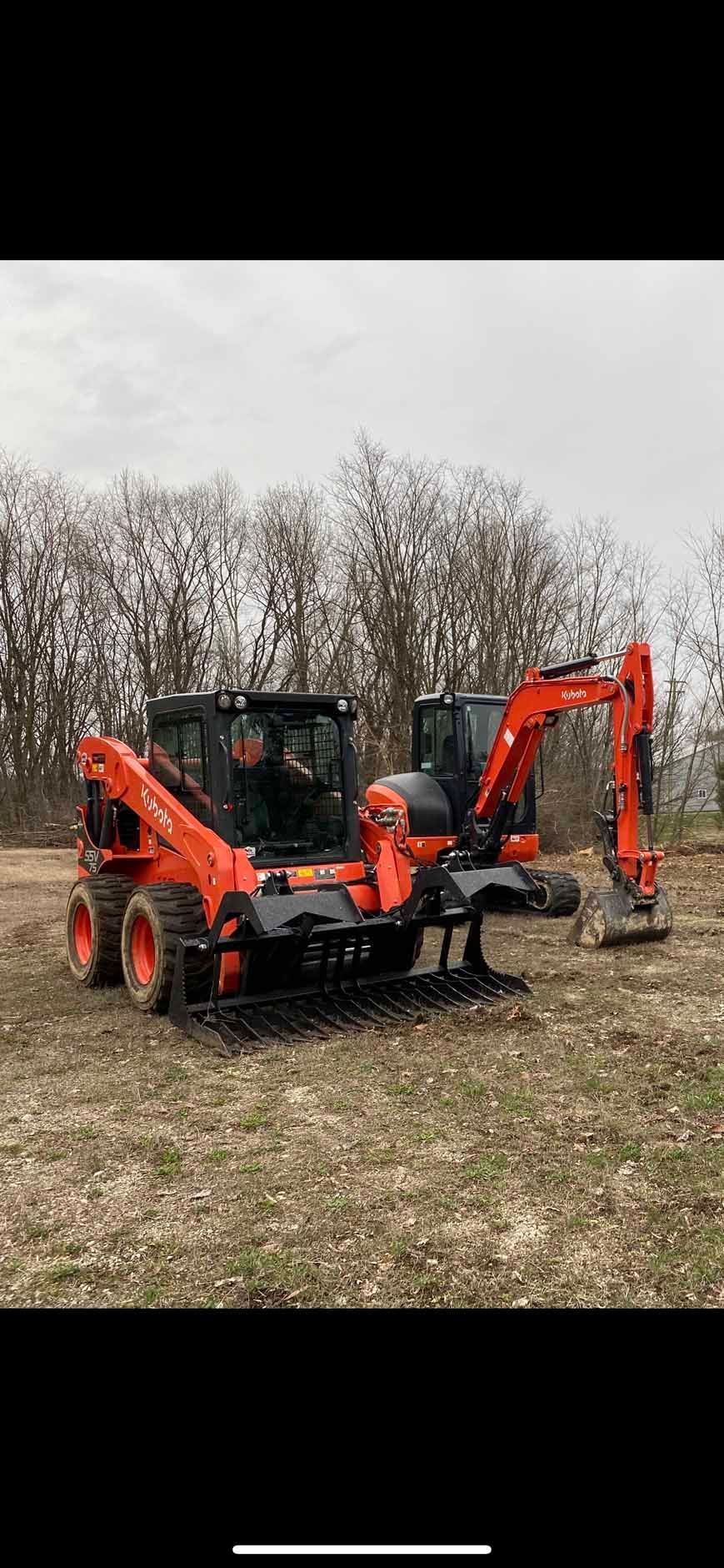 Orange Kubota skid steer with a grappler attachment parked next to a Kubota excavator in a field.