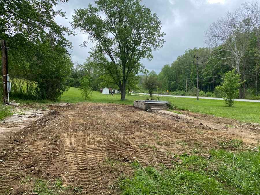 An open, freshly graded dirt construction site with tire tracks, leading to a small concrete set of stairs in a rural area.