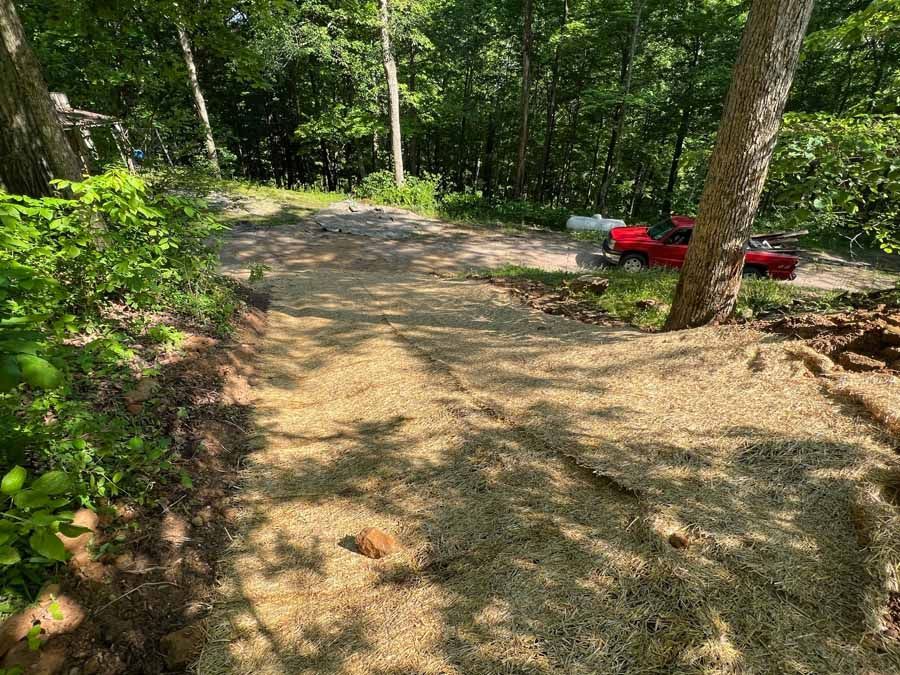 A sloped path covered in straw erosion control matting leads down toward a dirt area with a parked red pickup truck.