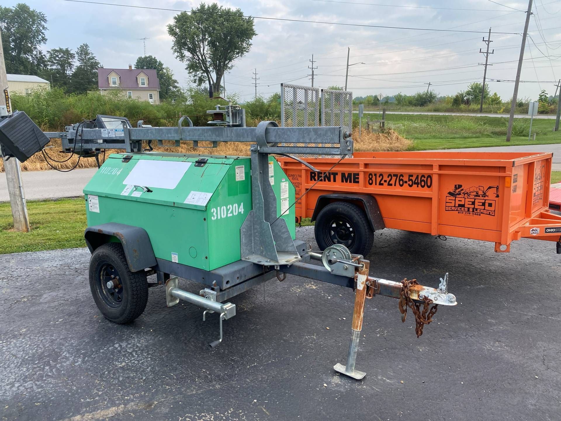 A green portable light tower trailer parked next to an orange 