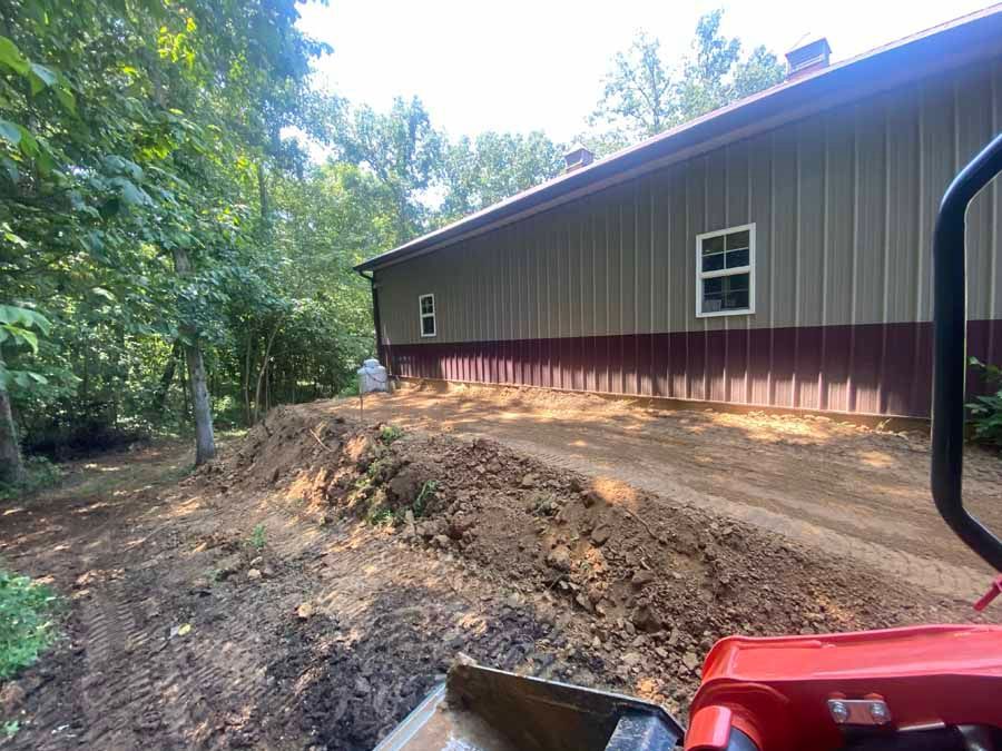 A view from a red tractor showing freshly graded dirt and a metal building with tan upper walls and dark red skirting.