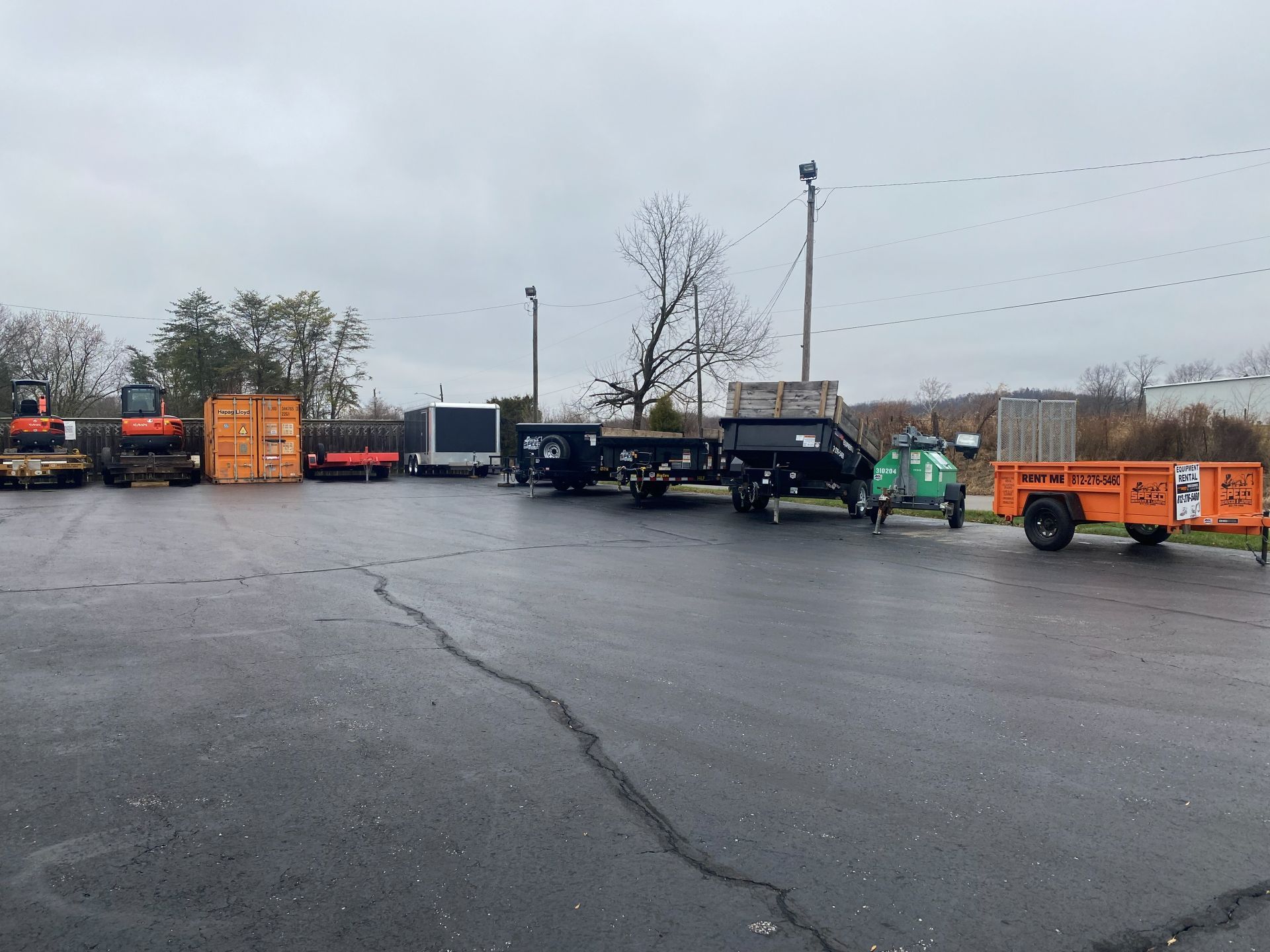 A parking lot filled with various construction equipment, including excavators, trailers, and dump trailers.