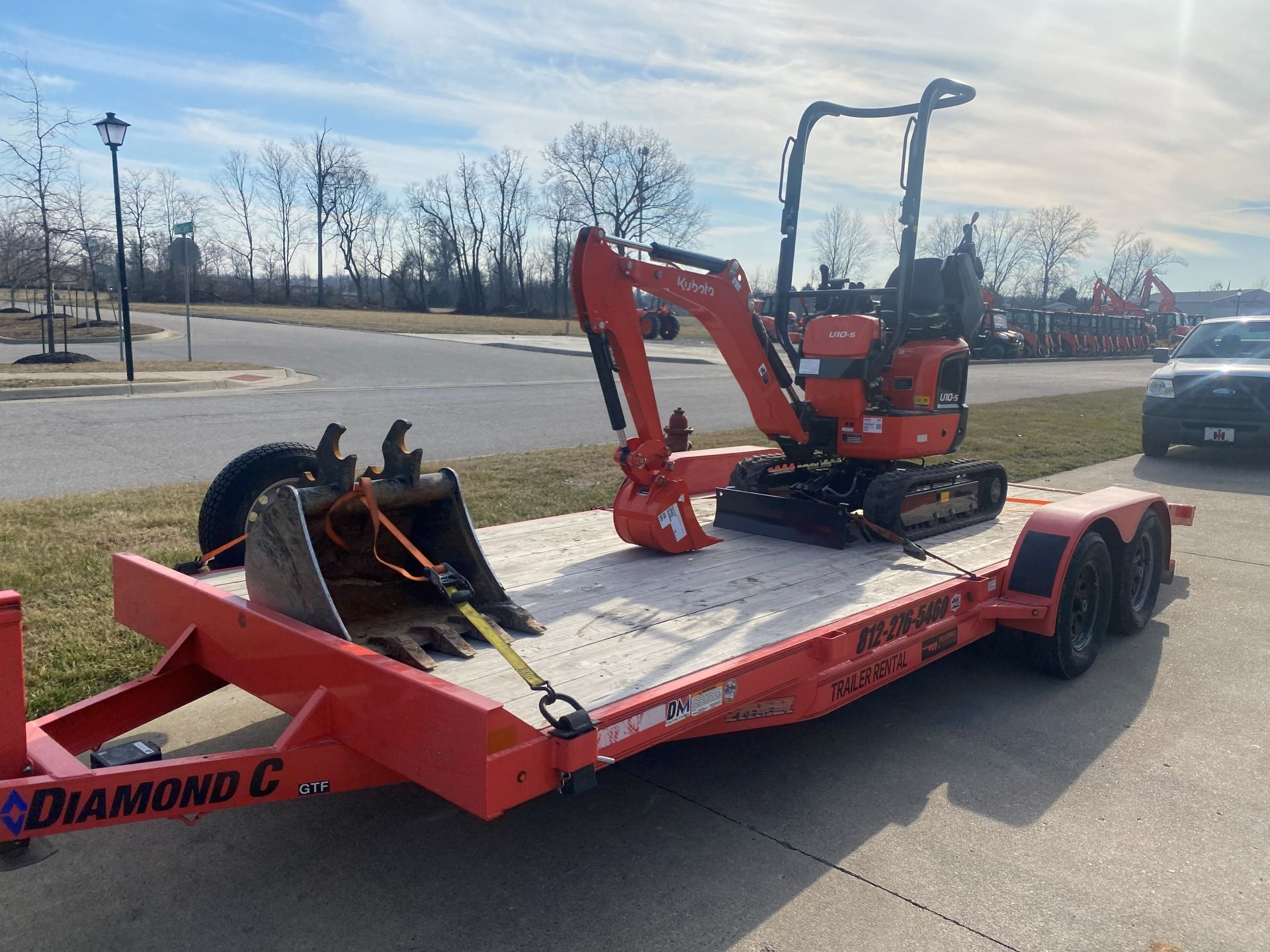 An orange Kubota mini excavator and a separate excavator bucket are secured on a flatbed Diamond C trailer.