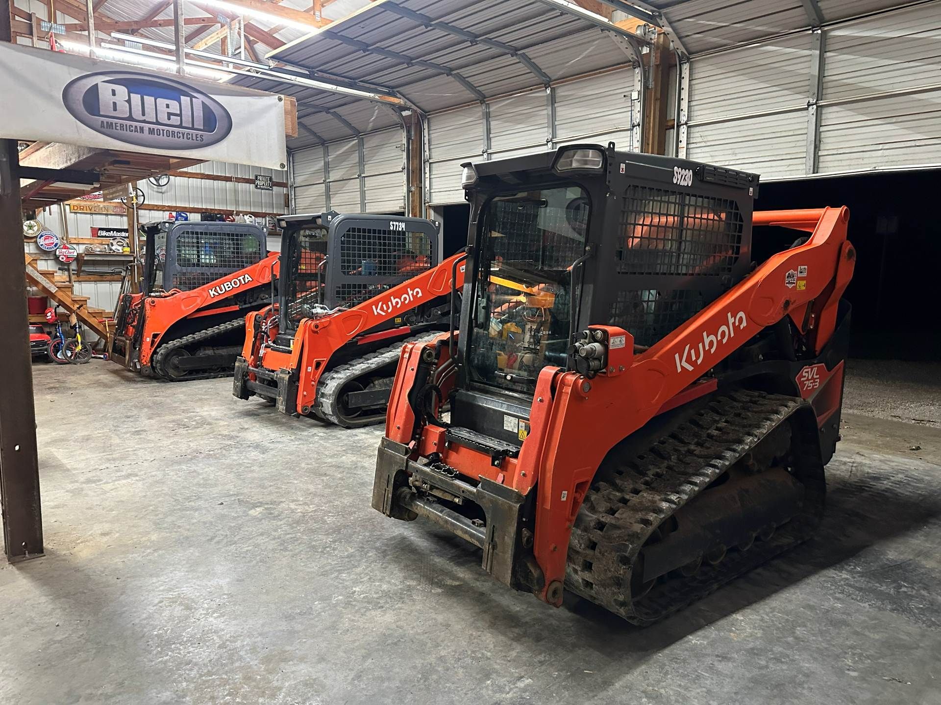 Three orange Kubota compact track loaders parked in a row inside a workshop with a 