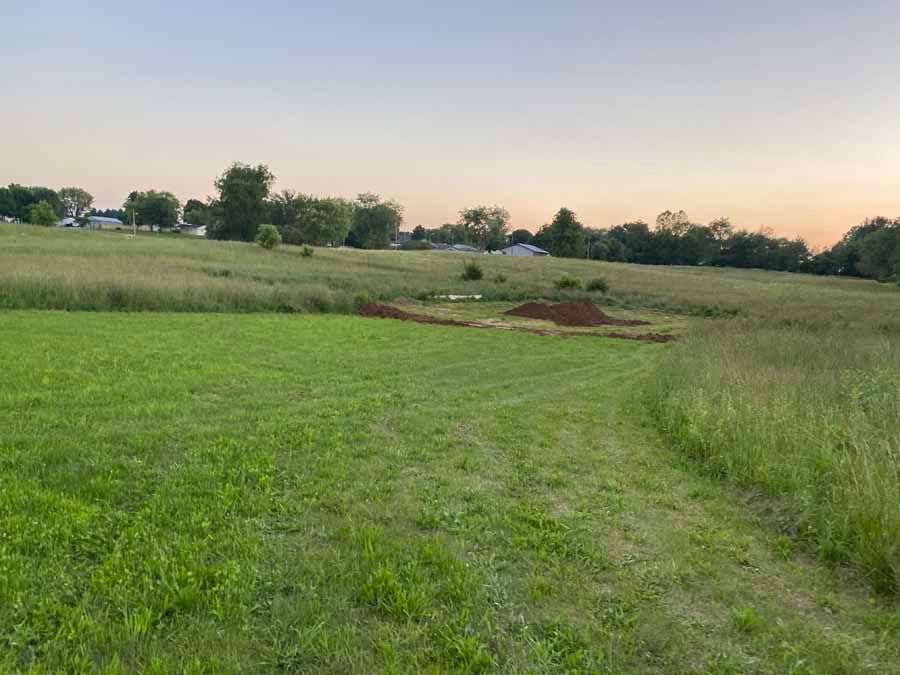 A grassy field under a sunset sky, featuring a small dirt mound and a patch of disturbed earth in the center.