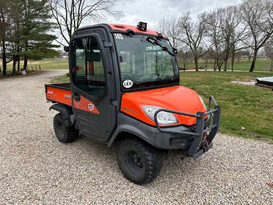 Orange Kubota RTV utility vehicle with an enclosed cab, parked on a gravel driveway outdoors.