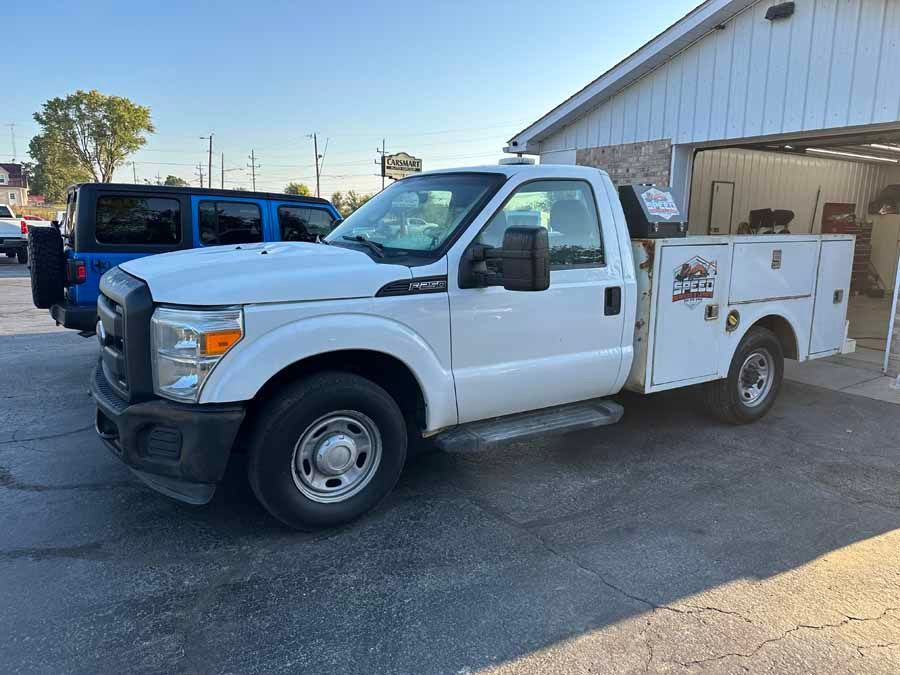 A white Ford F-250 utility truck parked on a paved lot with a blue SUV visible in the background.