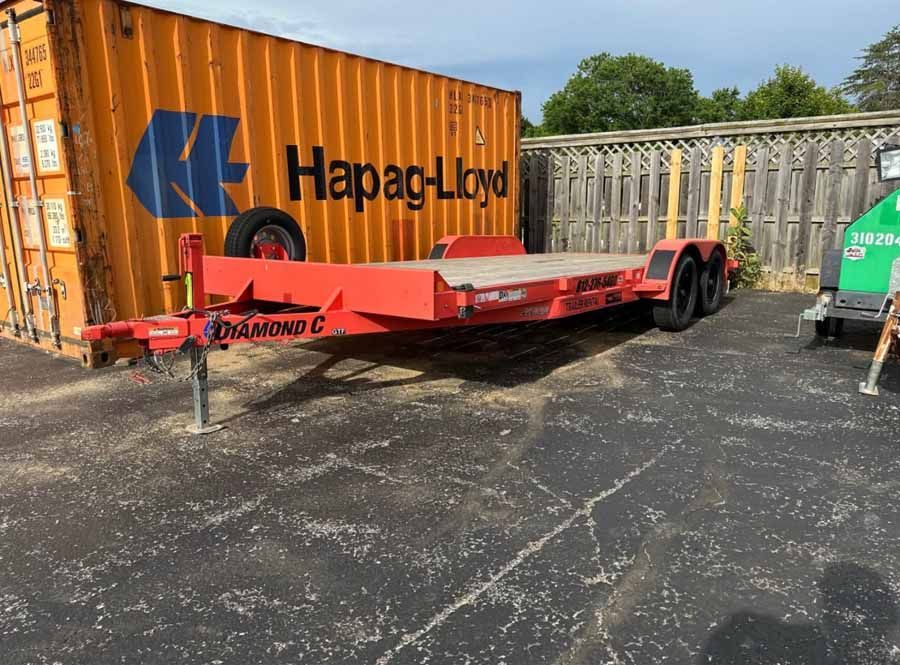 A bright red Diamond C equipment trailer parked next to a large orange Hapag-Lloyd shipping container.