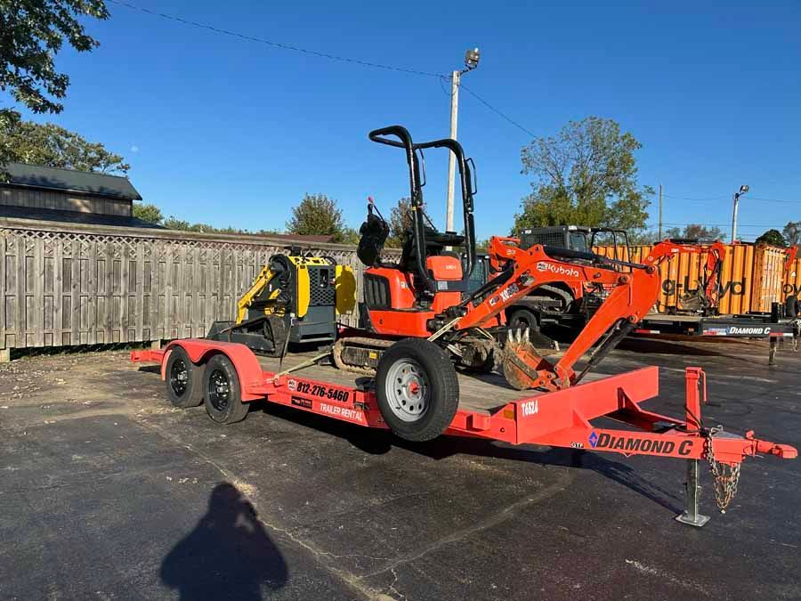 An orange Kubota excavator and a small yellow loader parked on an orange flatbed trailer outdoors.