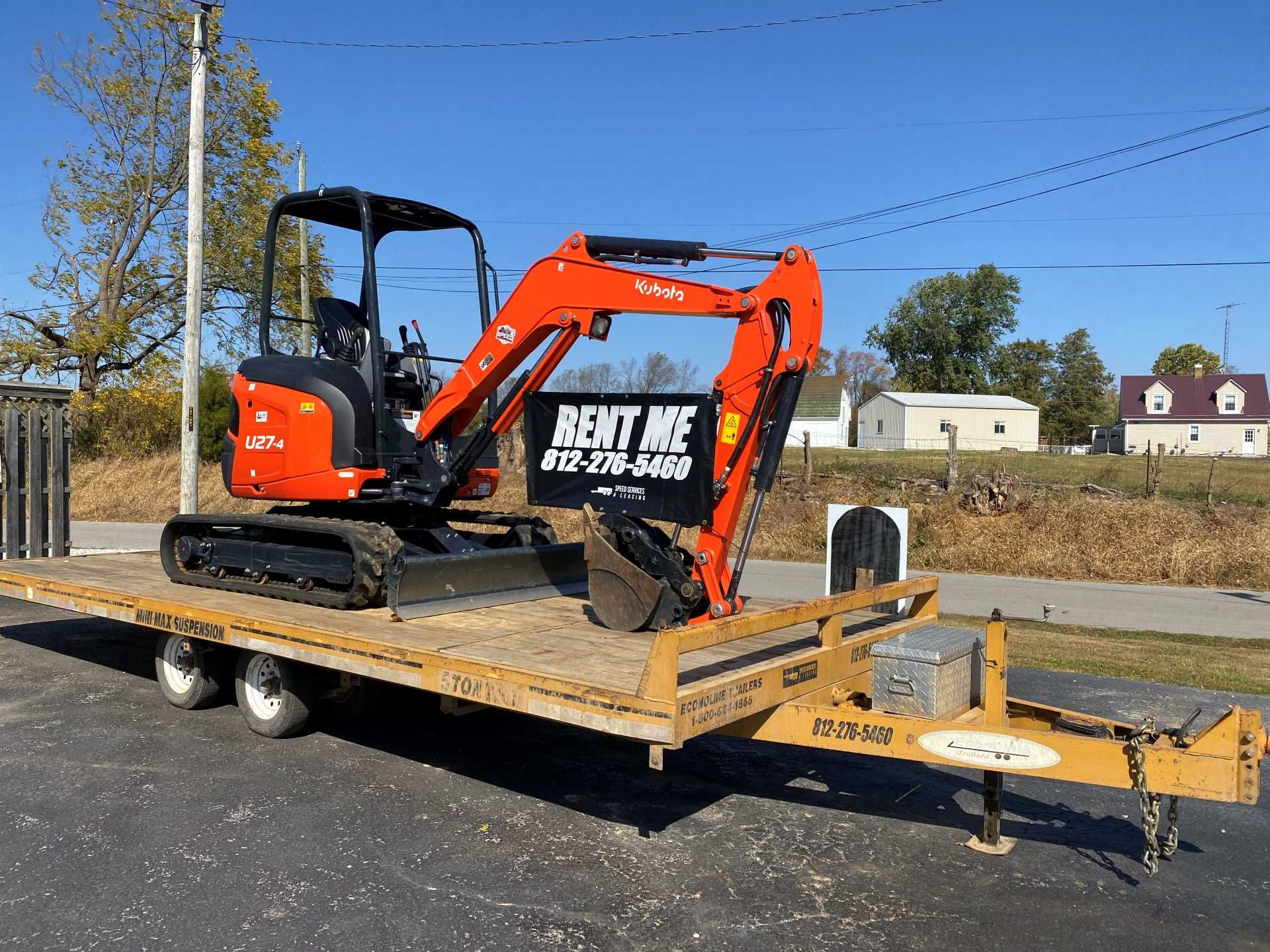An orange Kubota excavator sits on a flatbed trailer outdoors, featuring a 