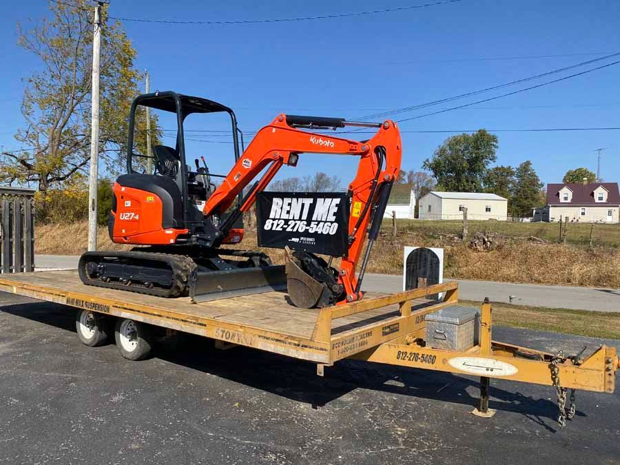 A bright orange Kubota mini excavator sits on a flatbed trailer outdoors, featuring a 