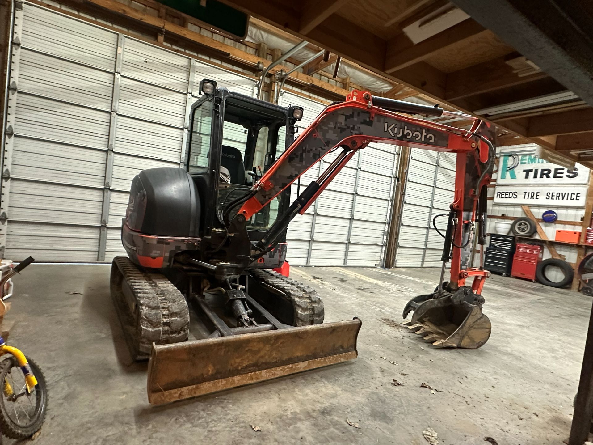 Orange and black Kubota excavator with a grapple bucket parked inside a garage.