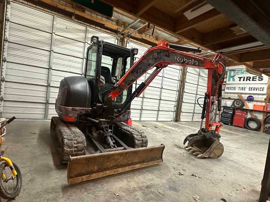 An orange Kubota excavator with a bucket attachment sits inside a garage with white bay doors.