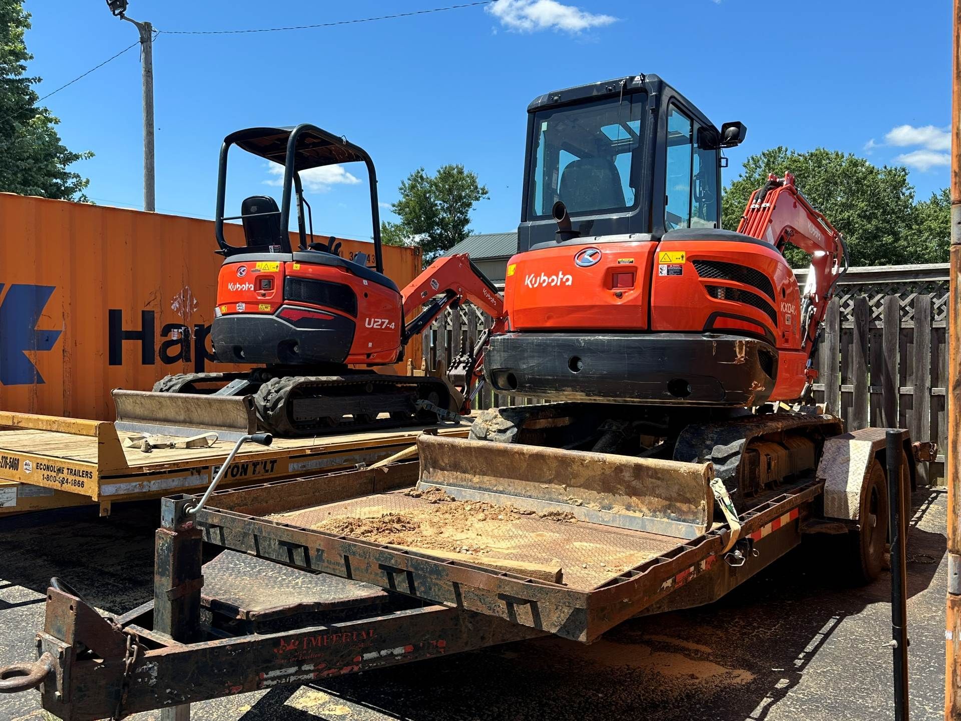 Two orange Kubota excavators parked on a flatbed trailer outdoors on a sunny day.