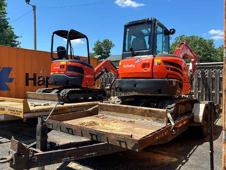 Two orange Kubota excavators parked on flatbed trailers under a bright blue sky.