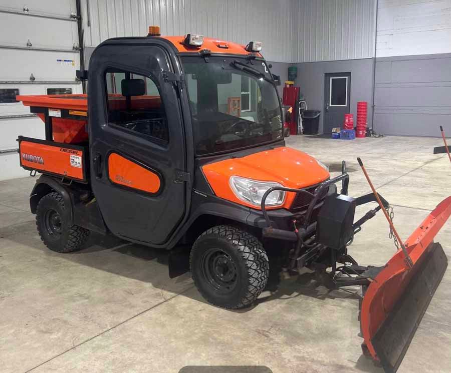 Orange and black utility vehicle with a snow plow and salt spreader parked inside a garage.