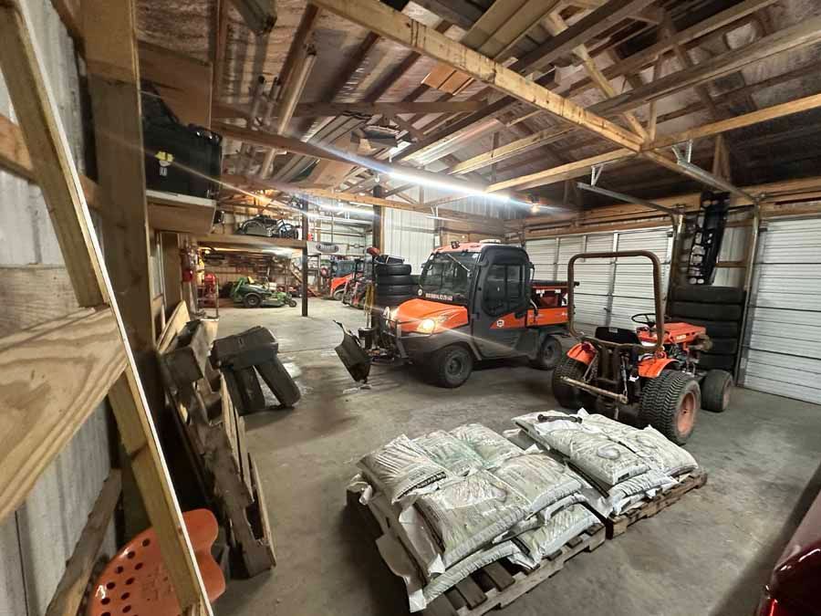 An interior view of a garage housing two orange utility vehicles and pallets of bagged materials on a concrete floor.