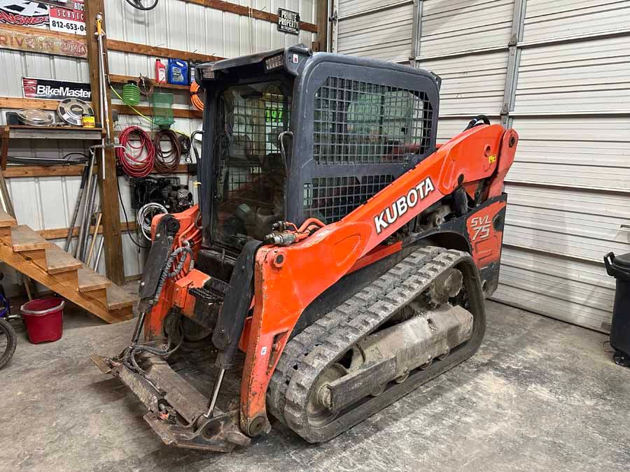 Orange Kubota compact track loader parked inside a warehouse or garage with metal walls.