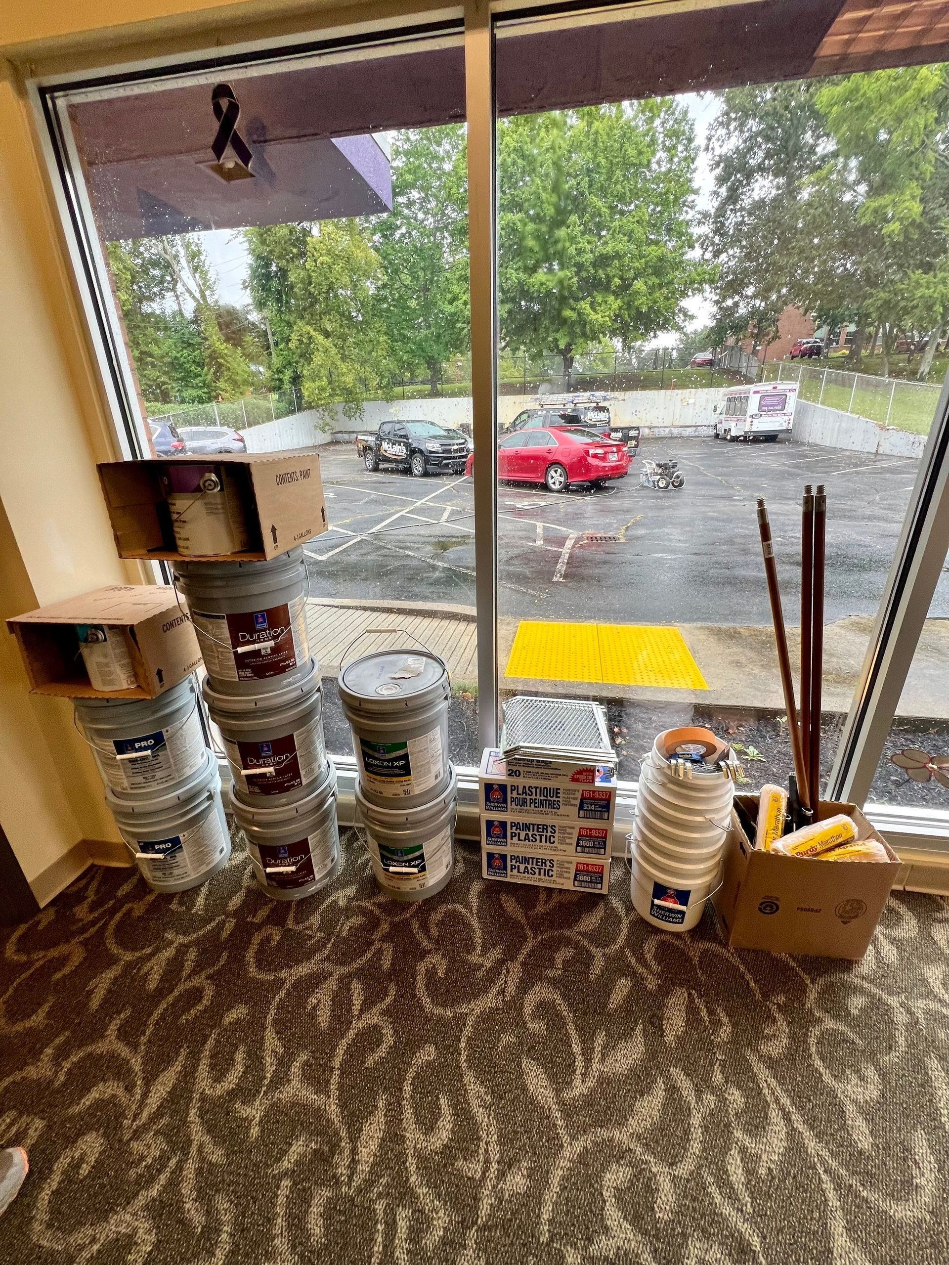 A room with buckets of paint and boxes in front of a window.