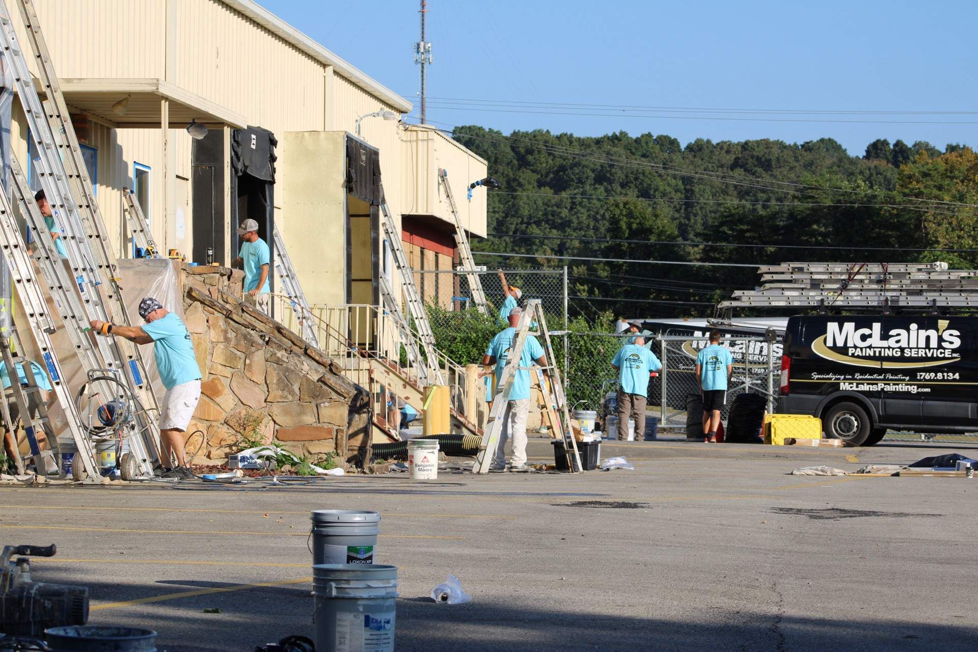 A group of people are painting a building in front of a mclain 's truck.