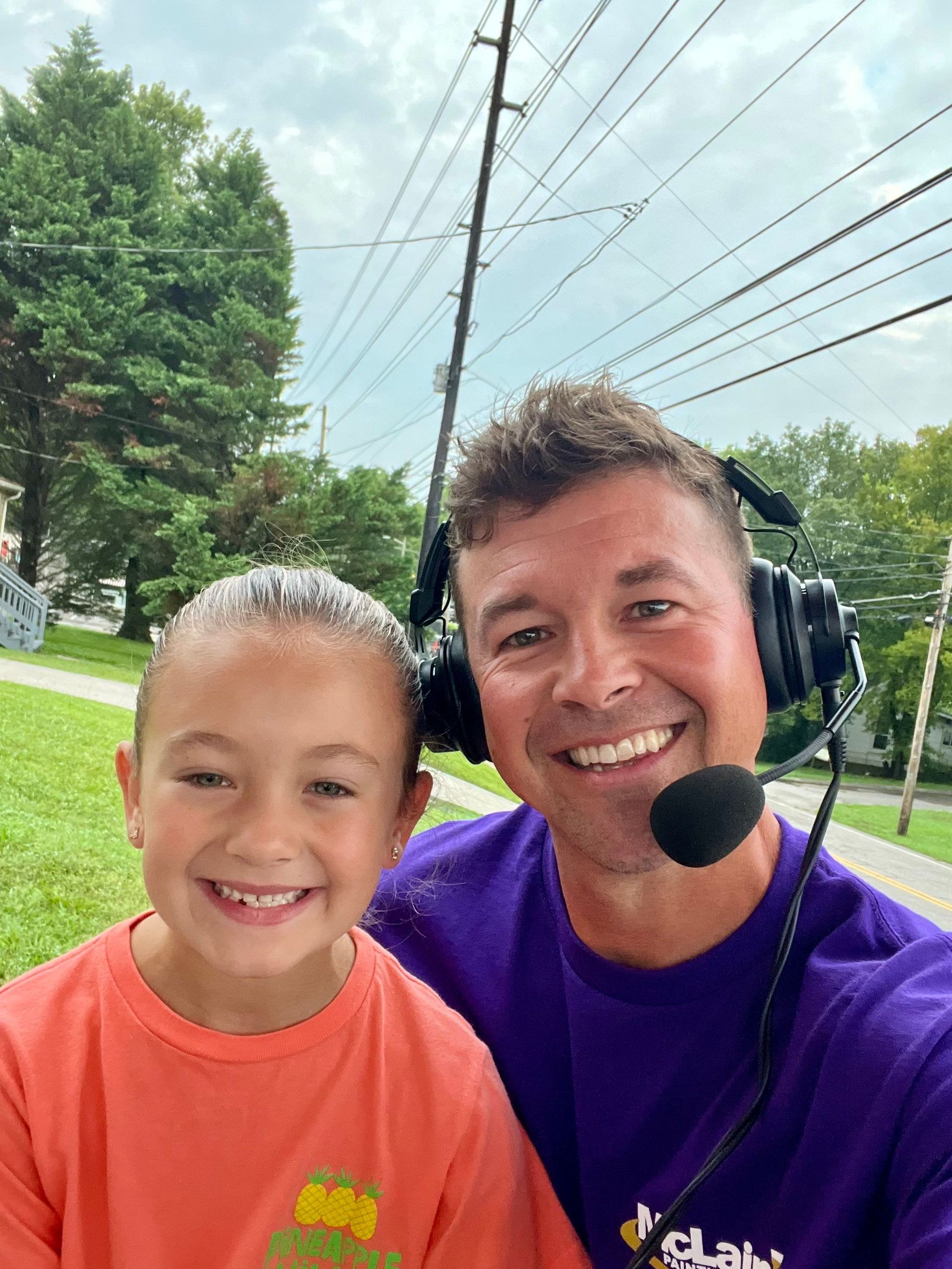A man wearing headphones and a microphone is sitting next to a little girl.