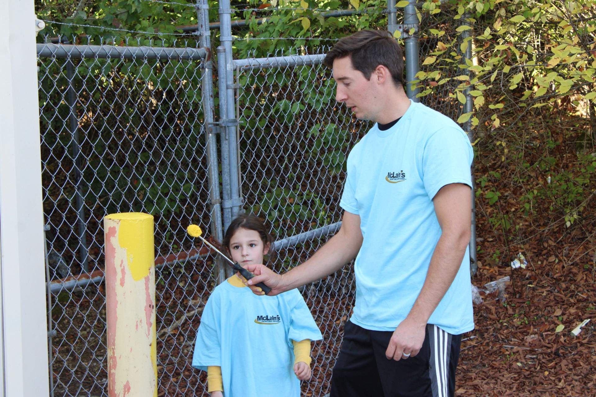A man and a little girl are standing in front of a chain link fence
