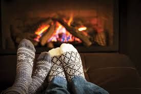 A couple of feet in socks sitting in front of a fireplace.
