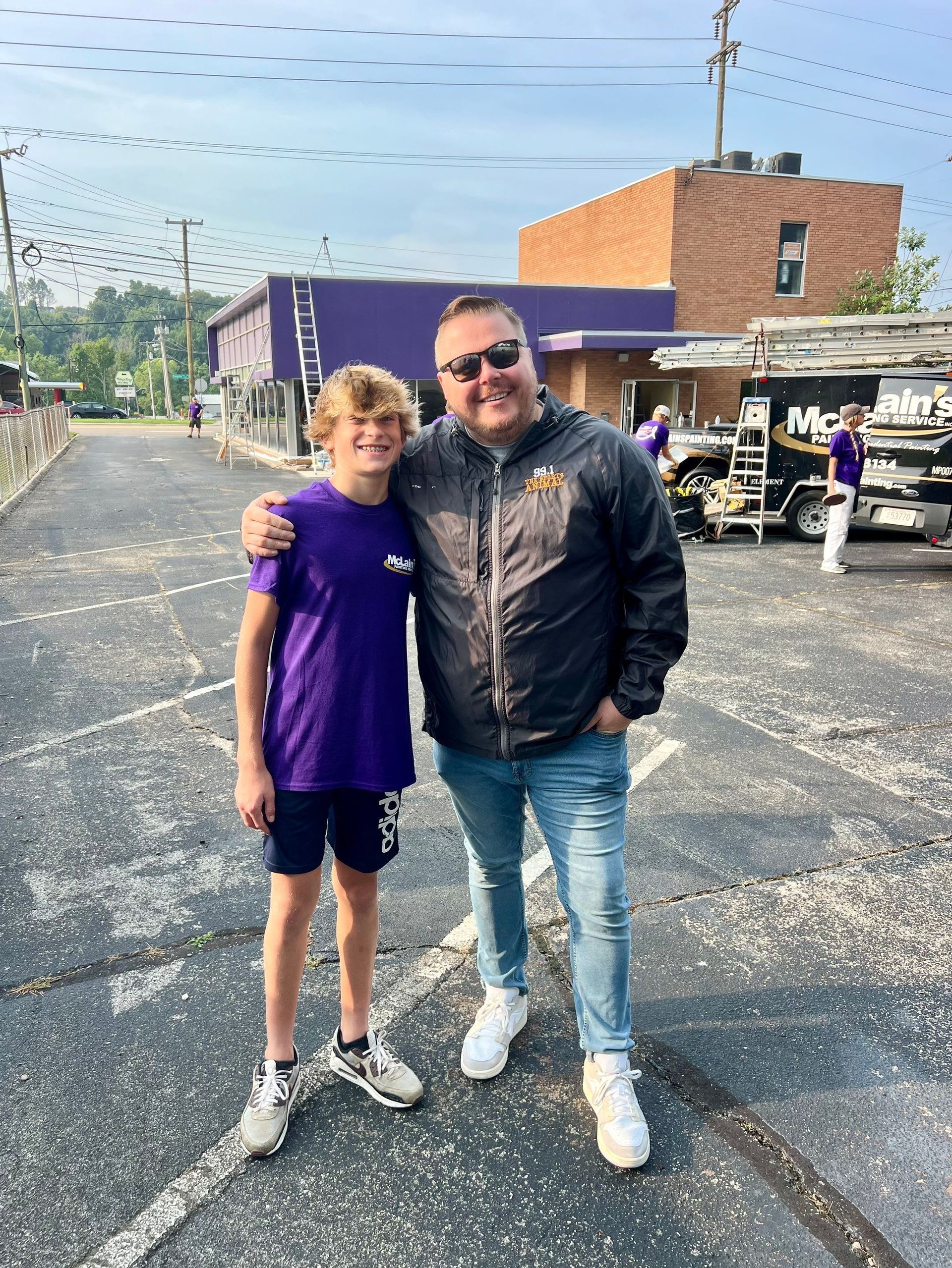 A man and a boy are posing for a picture in a parking lot.
