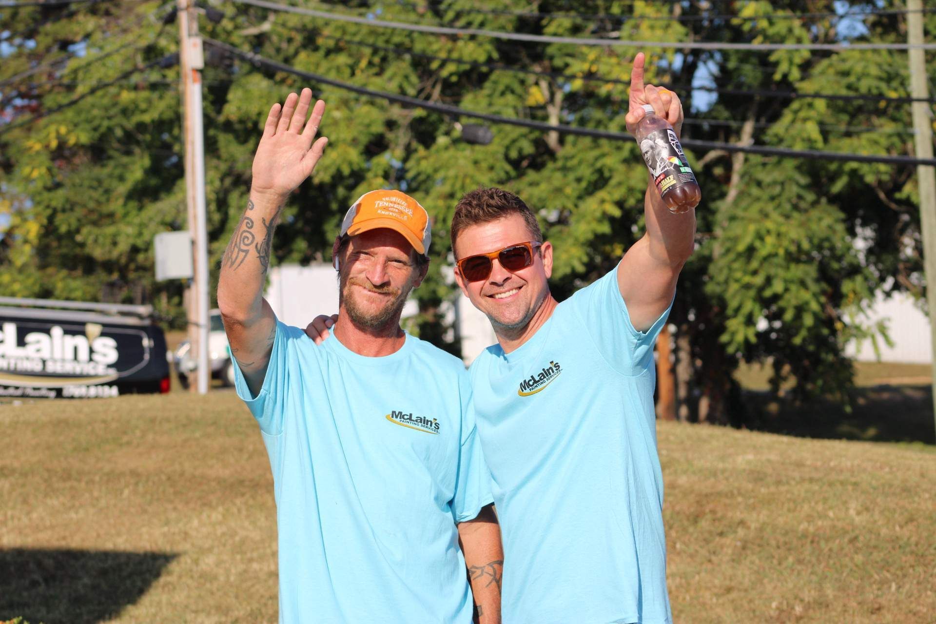 Two men in blue shirts are standing next to each other and waving.