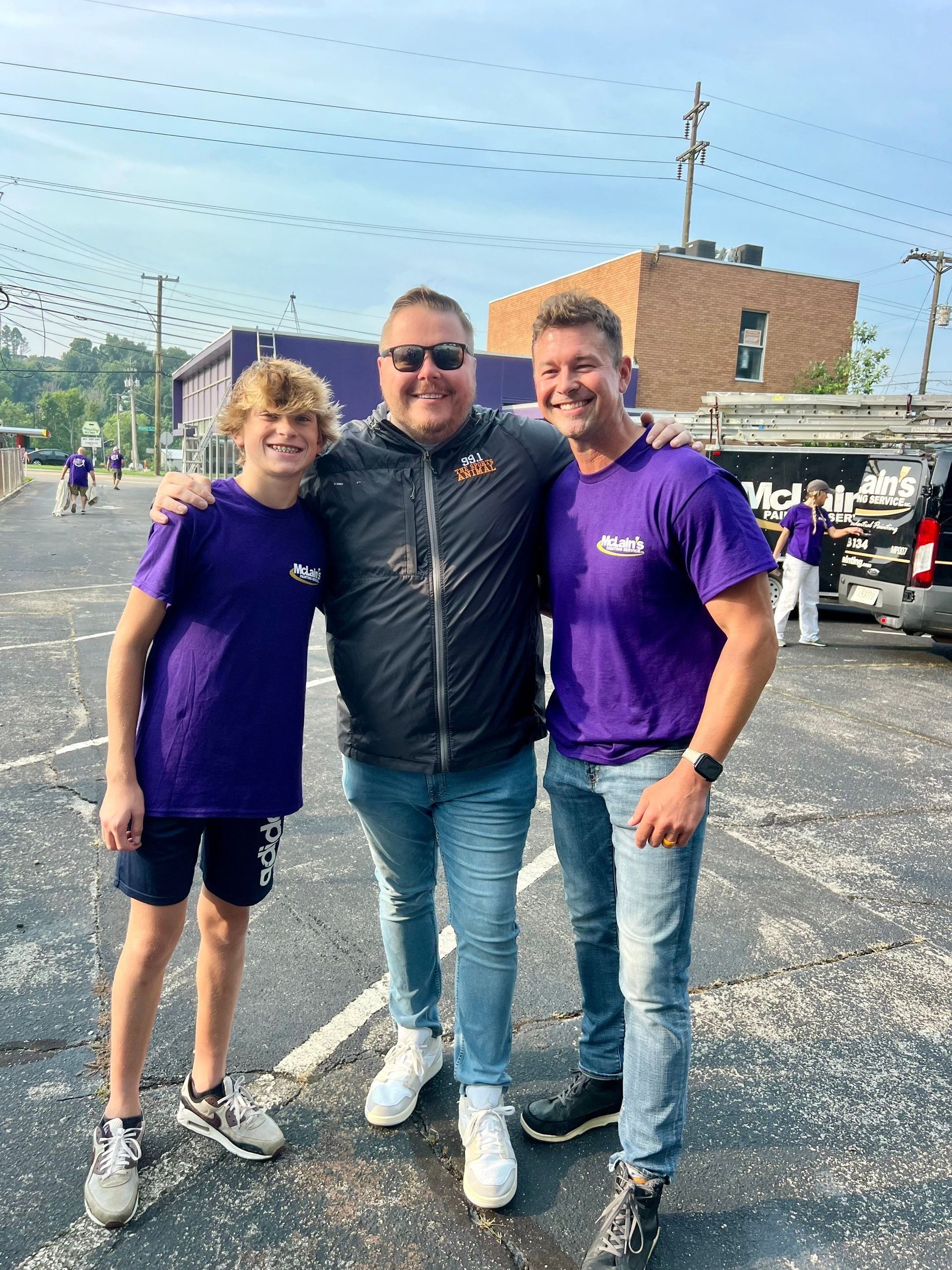 Three men are posing for a picture in a parking lot.