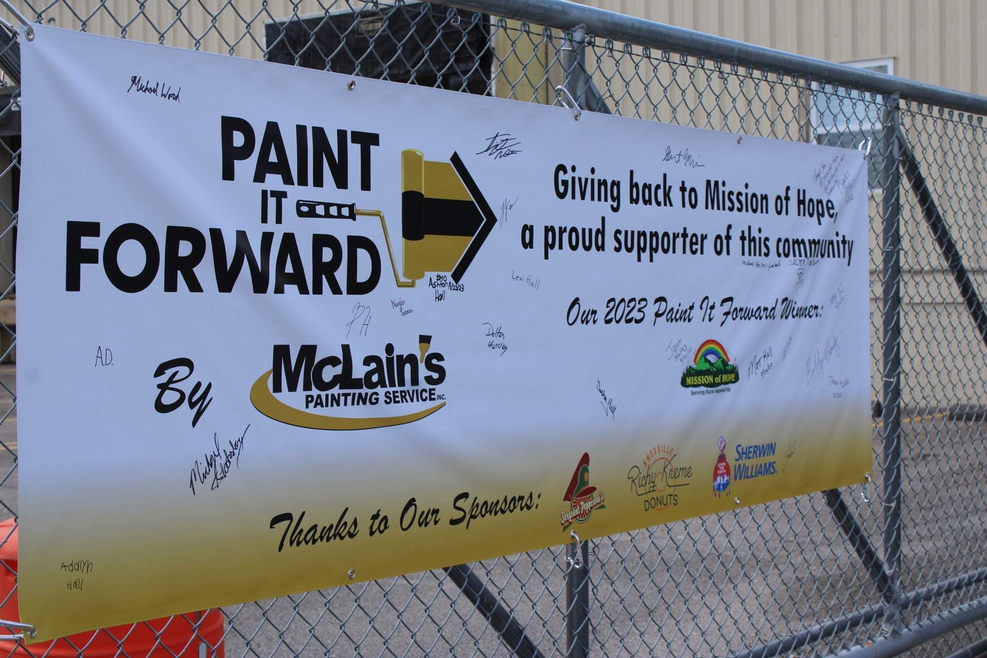 A sign on a chain link fence says paint it forward