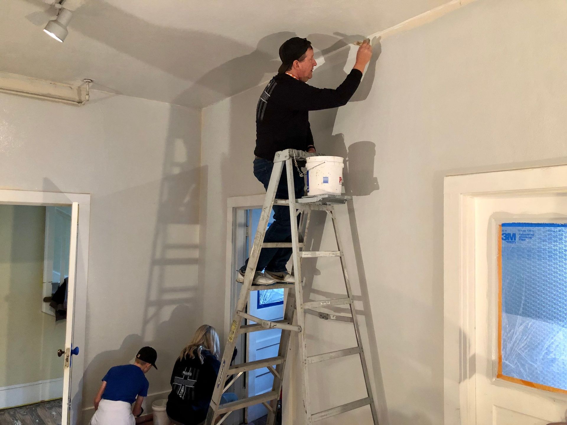 A man is standing on a ladder painting a wall.
