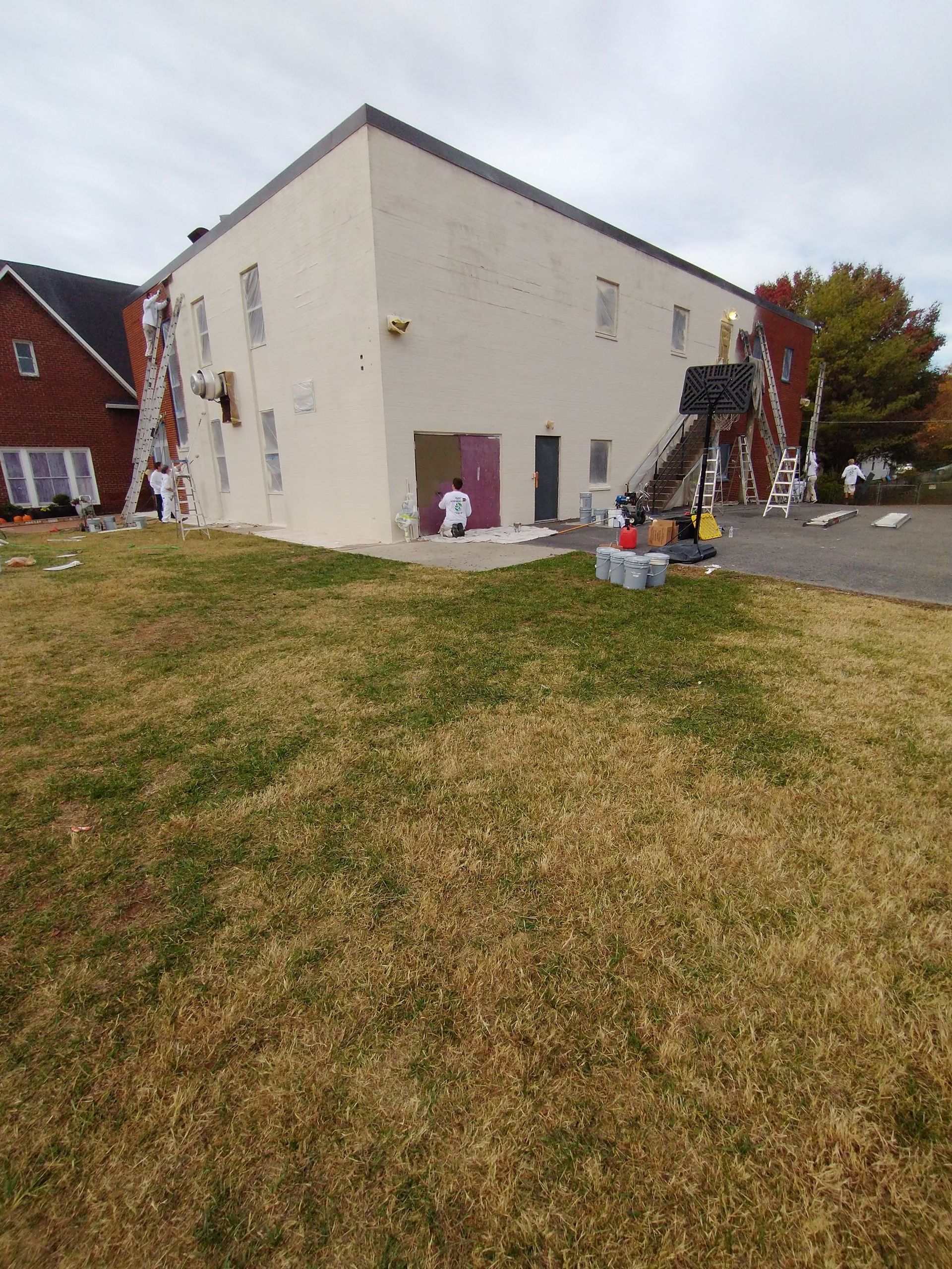 A large white building is being painted in a grassy area.